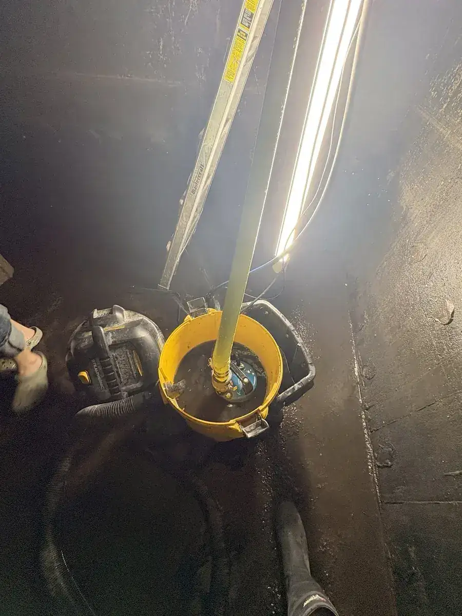 Cistern liner installation: Submersible pump seated in a bucket, discharge hose running up and out.
