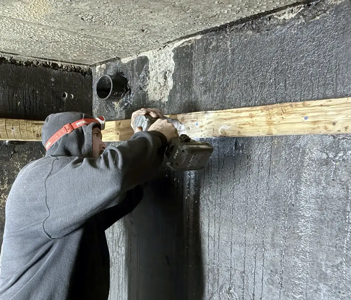 Cistern liner installation: Fastening the strapping into the concrete wall with a hammer drill.